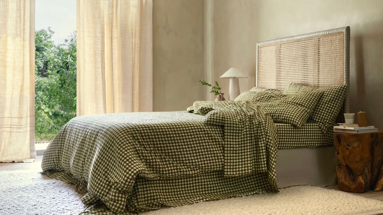 Botanical Green Gingham Sheet Set on a wooden bed frame against beige walls and beige curtains framing a window with a garden view. 