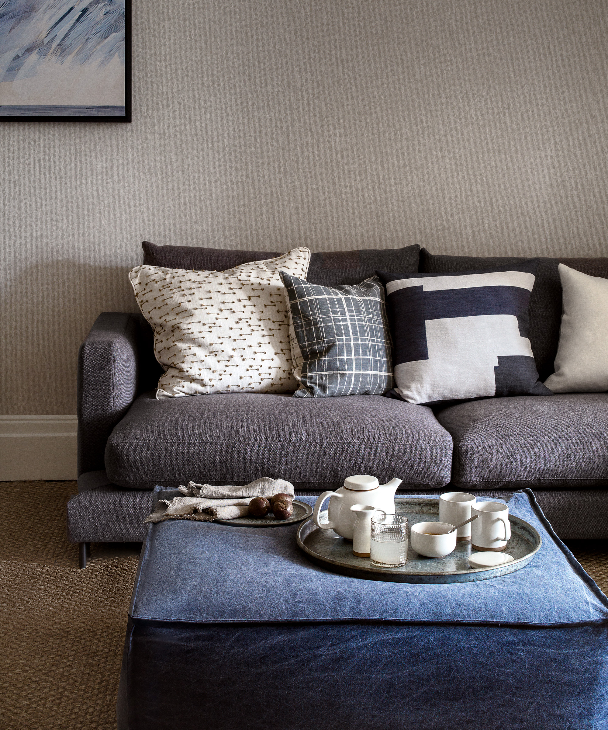A pale beige living room with charcoal grey sofa and different grey shades in the cushions.