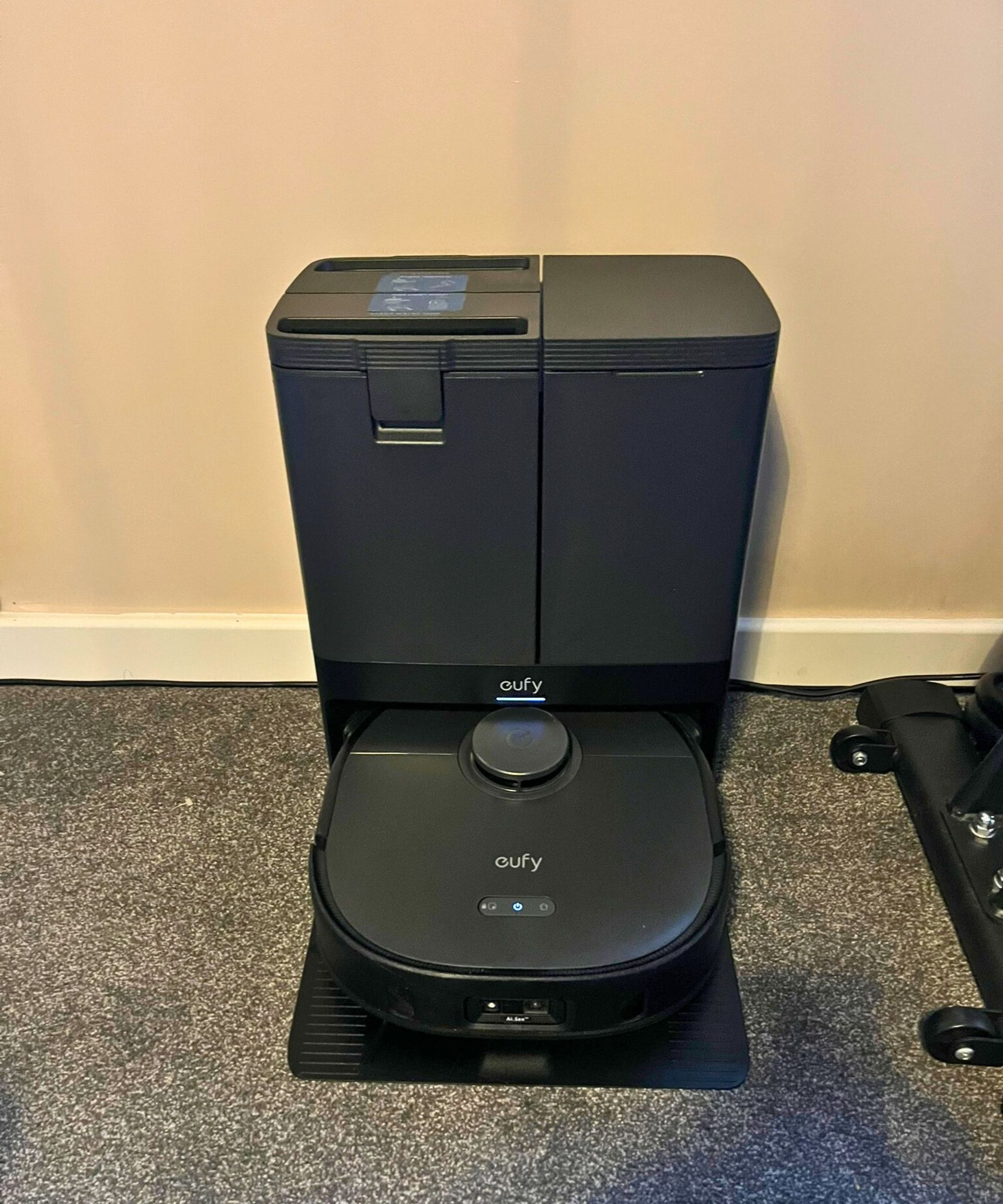 eufy X10 Pro Omni robot vacuum set up and charging in its base station in my bedroom which has gray carpet and neutral cream walls