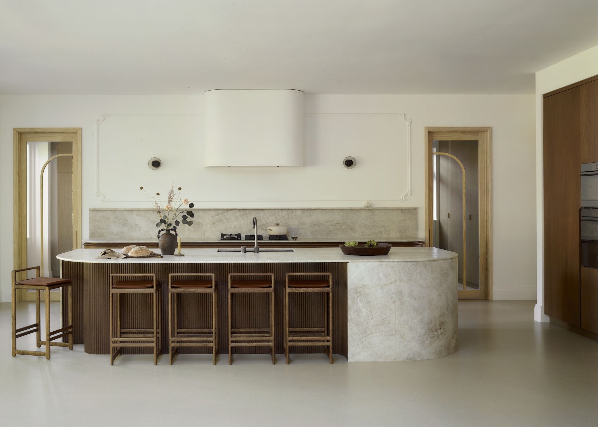 an oversized curved kitchen island in dark wood and stone with bar stools and pale concrete flooring