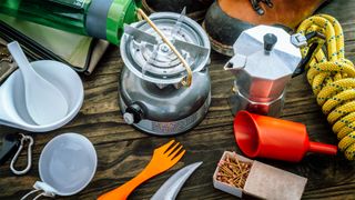 Camping utensils, a stove and coffee pot laid out on a table