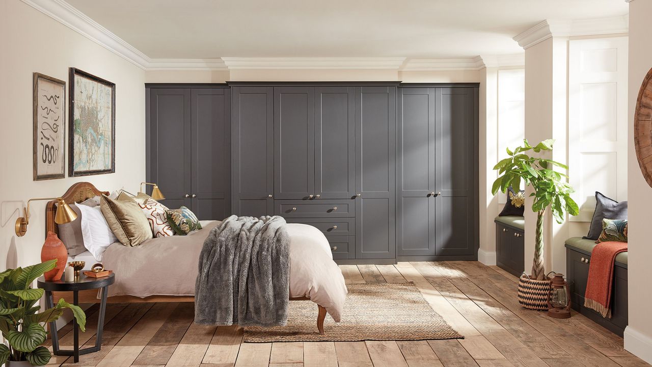 wall of grey fitted wardrobes in white and cream bedroom with wooden floors