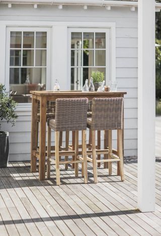 An outdoor decked space with outdoor table and four bar stool chairs