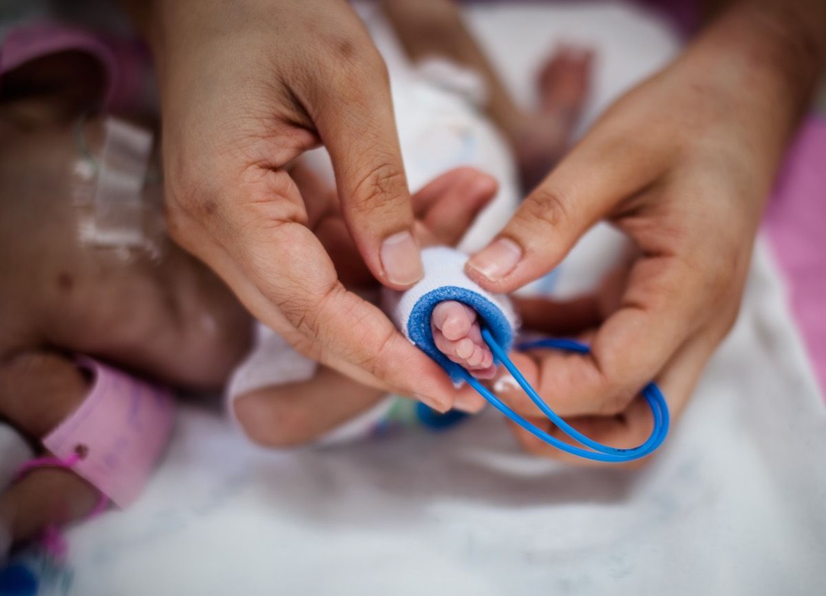 mother&#039;s hand holding feet of new born baby sick in incubator chamber in hospital