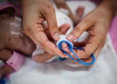 mother's hand holding feet of new born baby sick in incubator chamber in hospital
