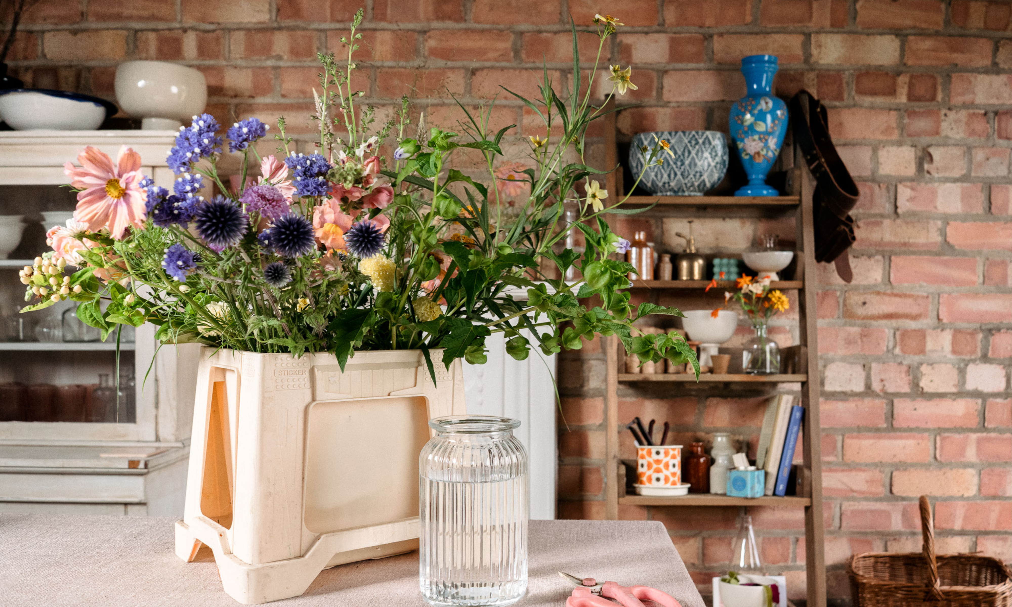Late summer garden flowers in floristry bucket with in glass vase on table