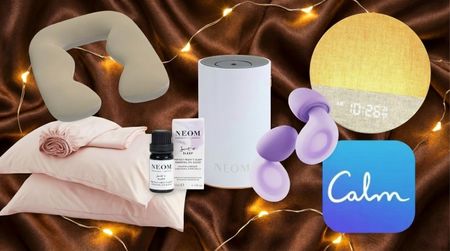 Pillows, NEOM diffuser, purple Loop earbuds, sunrise alarm clock and Calm app logo on brown silk background with fairy lights