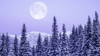 The full moon rises above snowcapped mountains.