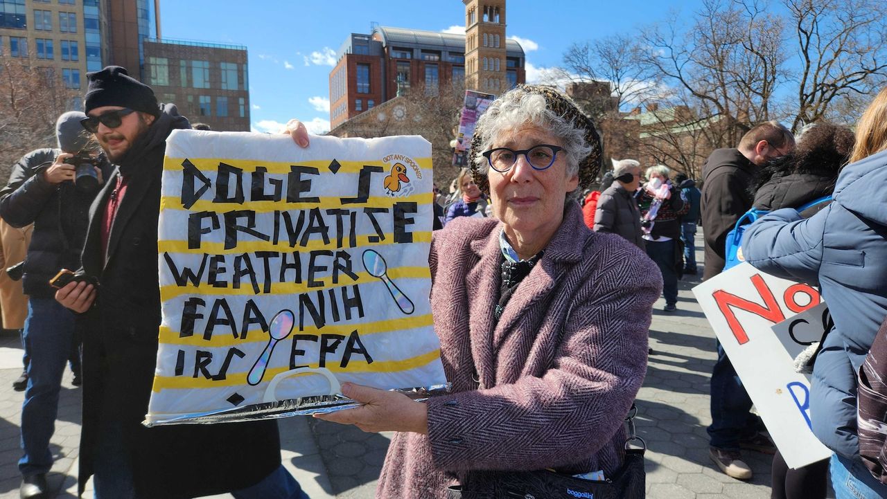 A woman holds a protest sign about Elon Musks' Department of Government Efficiency at the Stand Up For Science rally