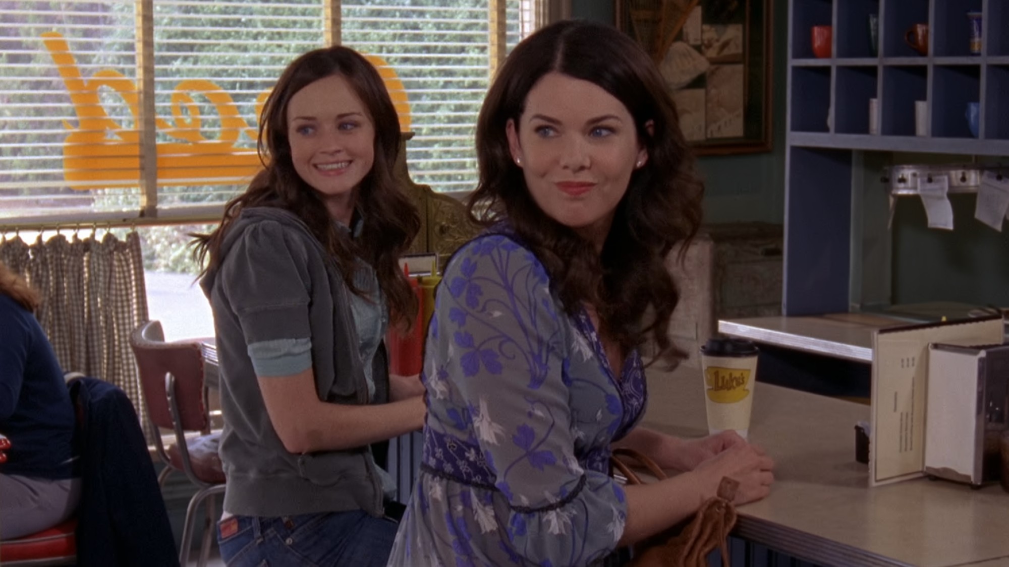 Rory and Lorelai at the counter and smiling while at Luke's on Gilmore Girls.