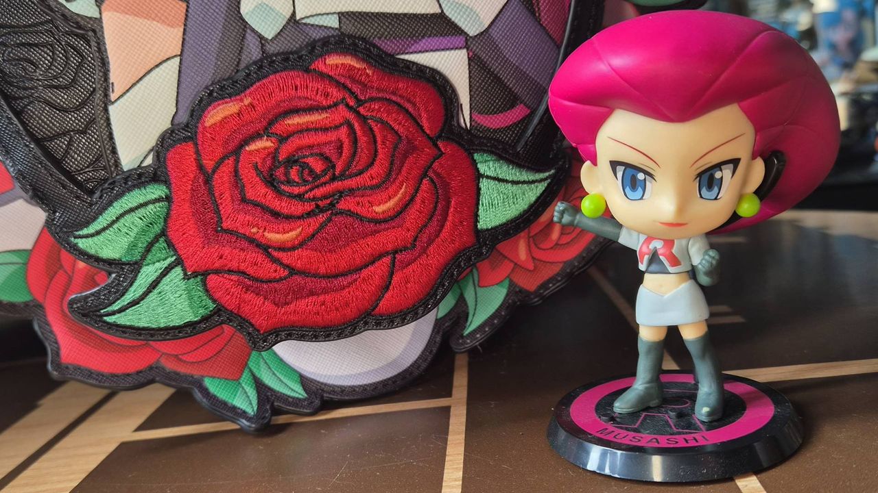 Close up of the rose on the front of the Team Rocket Cameo Mini Backpack with a Jessie toy to its side.