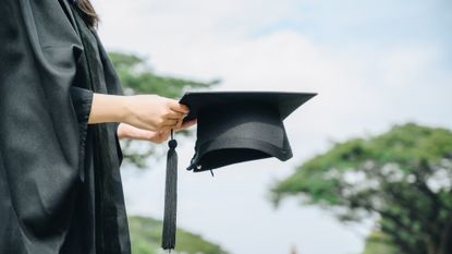 Student wearing graduation gown and holding a graduation cap