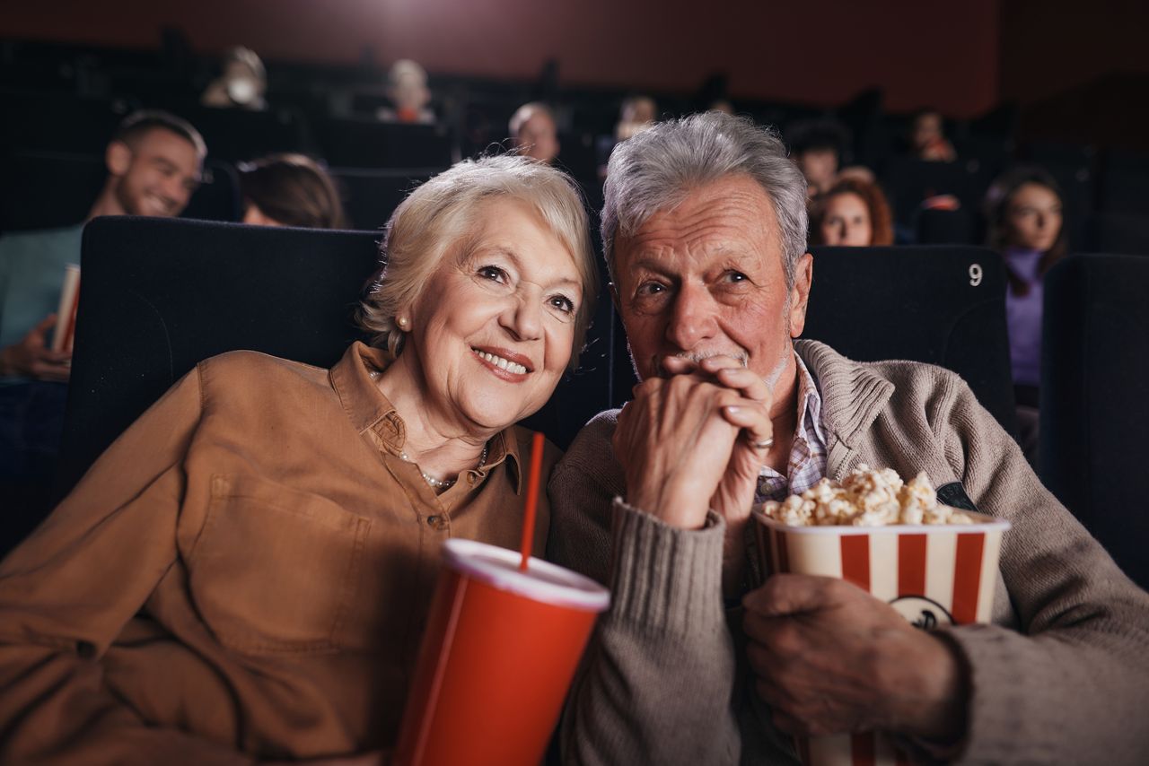 Happy mature couple holding hands while watching a movie in cinema.