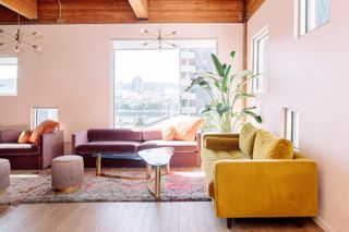 A pink livingroom with velvet sofas and a large window over a cityscape