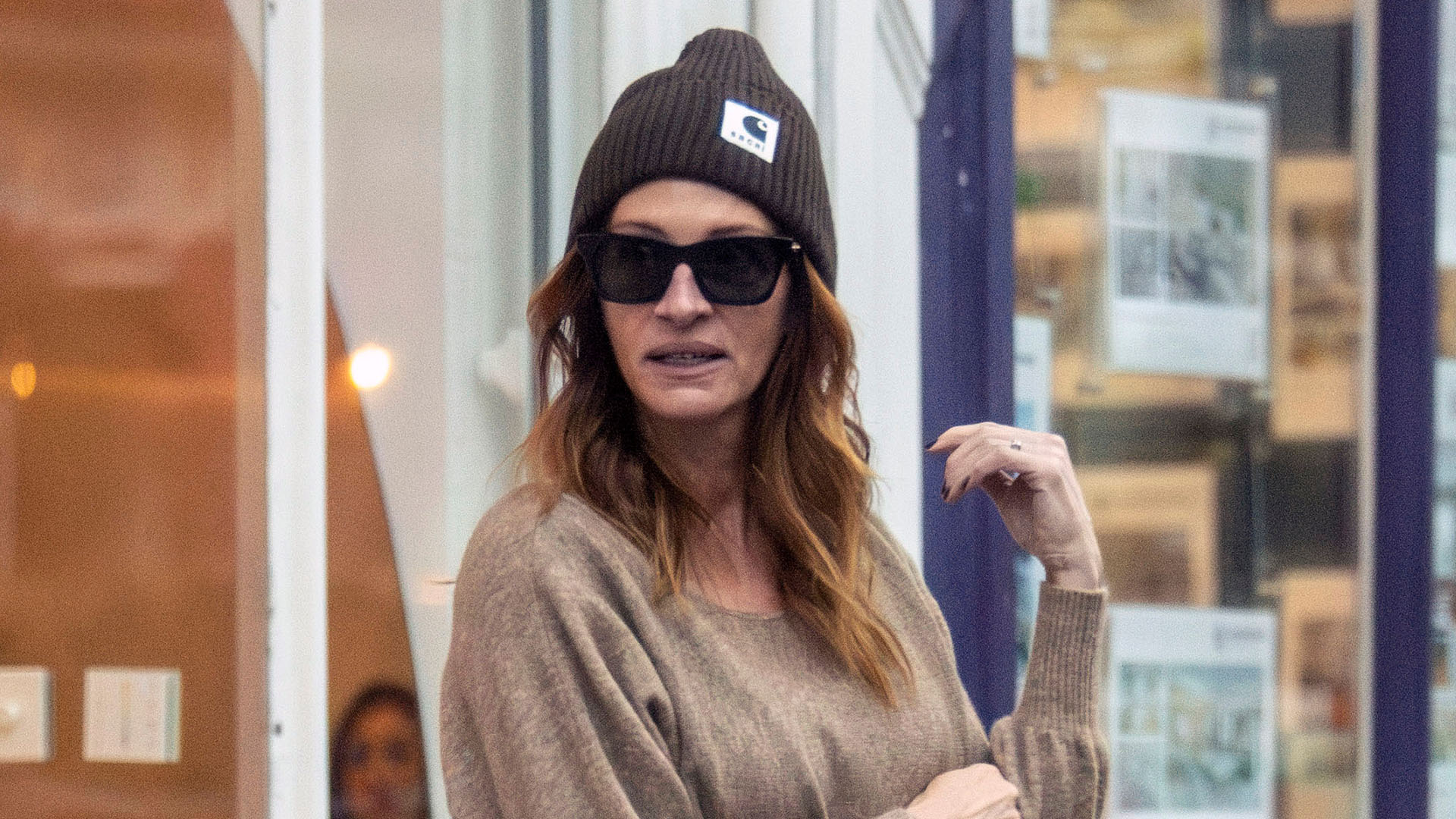 Julia Roberts wearing a brown sweater, dark brown pants, black flats, a navy bag, and a brown knit hat.