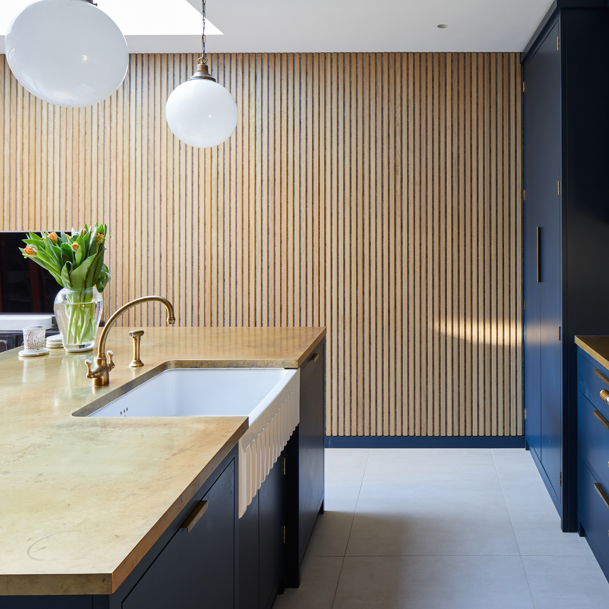 a dark blue kitchen with a wooden vertical paneling on the adjacent wall and two pendant shades hanging over the kitchen island