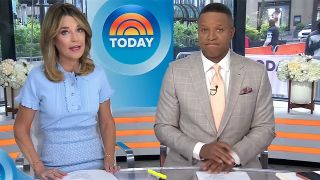 Savannah Guthrie and Craig Melvin sit at the desk on The Today show. She has on a blue dress and he has on a grey suit and peach tie.