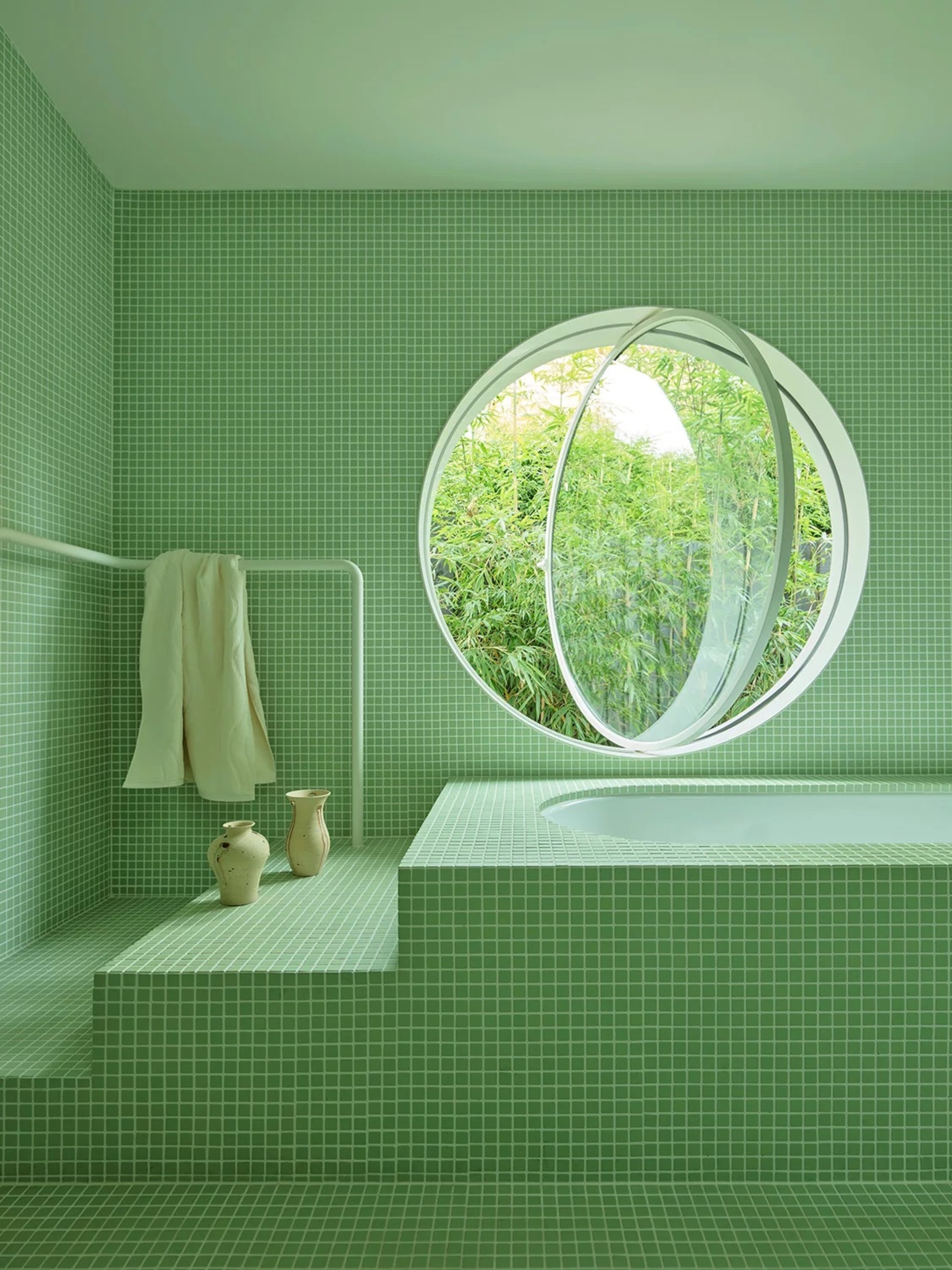 green color-drenched bathroom with green mosaic tiles, a step-up built-in bath, with hand rain, two ceramic vases, and a port-hole window