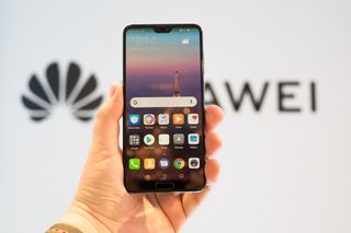 A hand holding a Huawei smartphone with the Huawei logo in the background