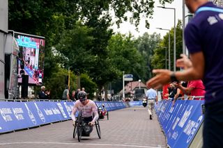 A man in a white long sleeve jersey and black helmet using a handcycle competes in a paracycling road race.