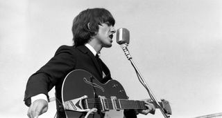 George Harrison plays outdoors with the Beatles in 1965. He is playing his Gretsch Country Gentleman, and as in his Beatles suit, wearing the mop-top haircut.