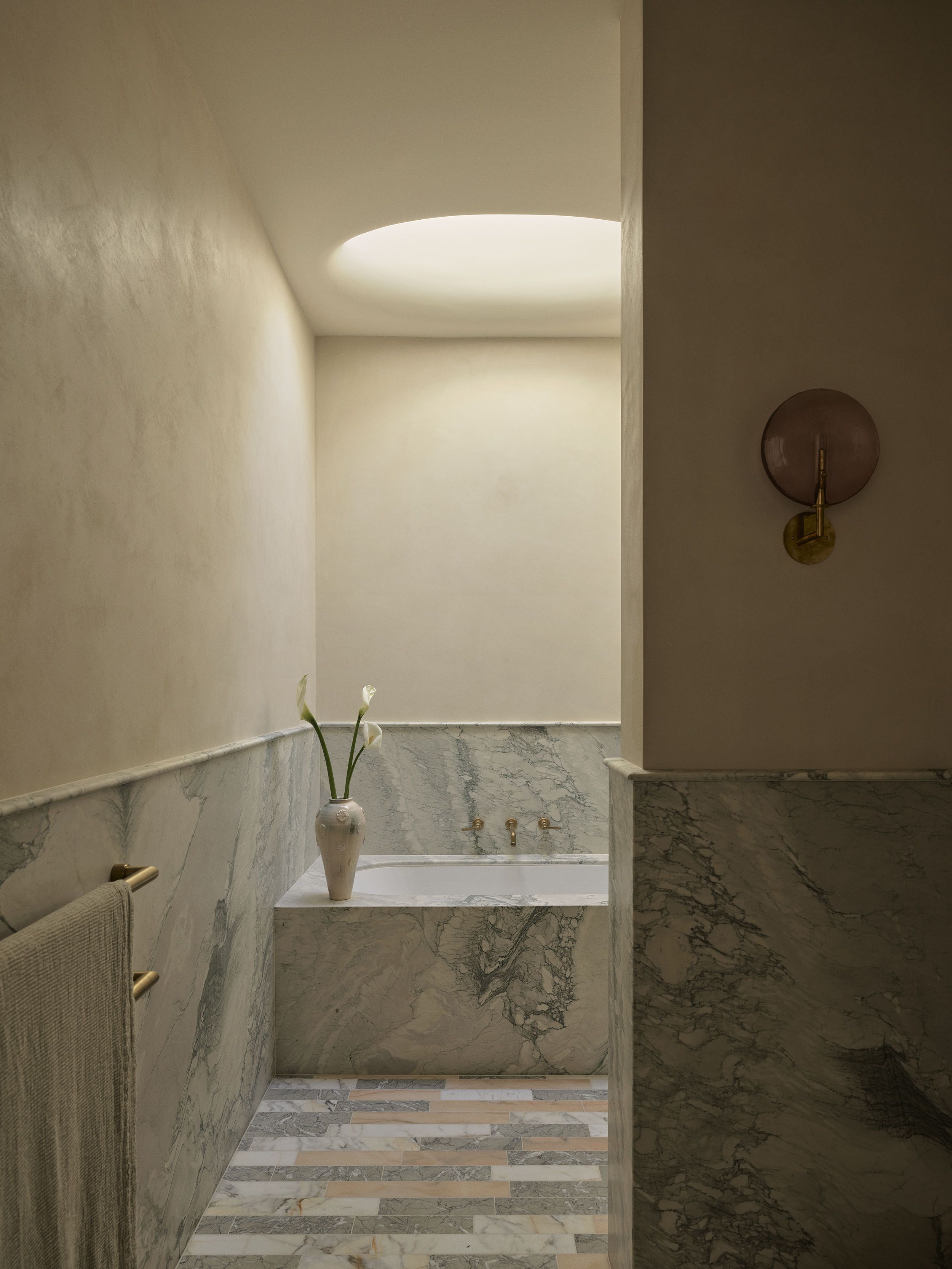 Marble-clad bathroom with a built-in bathtub, circular skylight and brushed brass fittings in Smac Studio's renovated Art Deco home in Woollahra, Sydney.