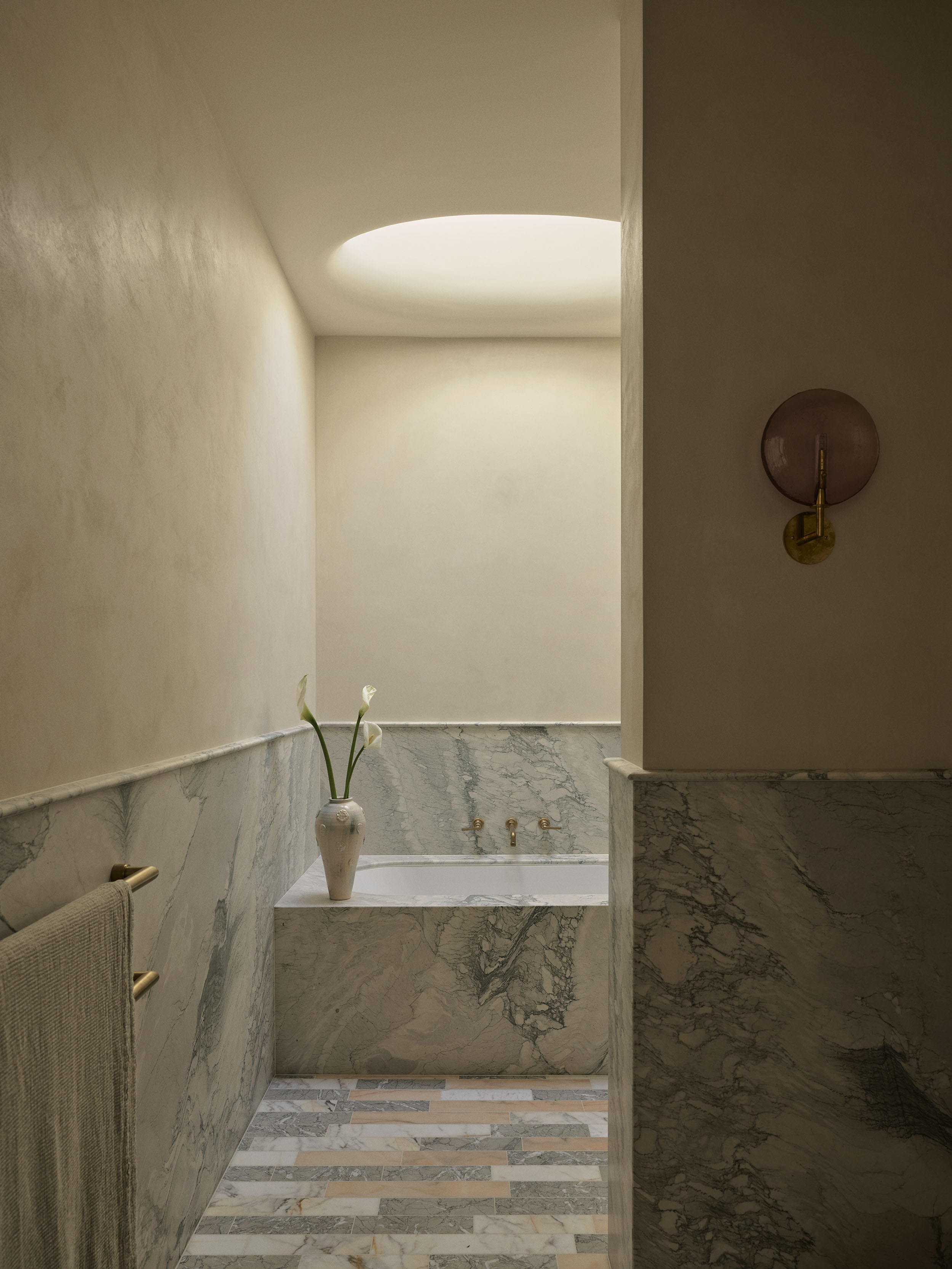 Marble-clad bathroom with a built-in bathtub, circular skylight and brushed brass fittings in Smac Studio's renovated Art Deco home in Woollahra, Sydney.