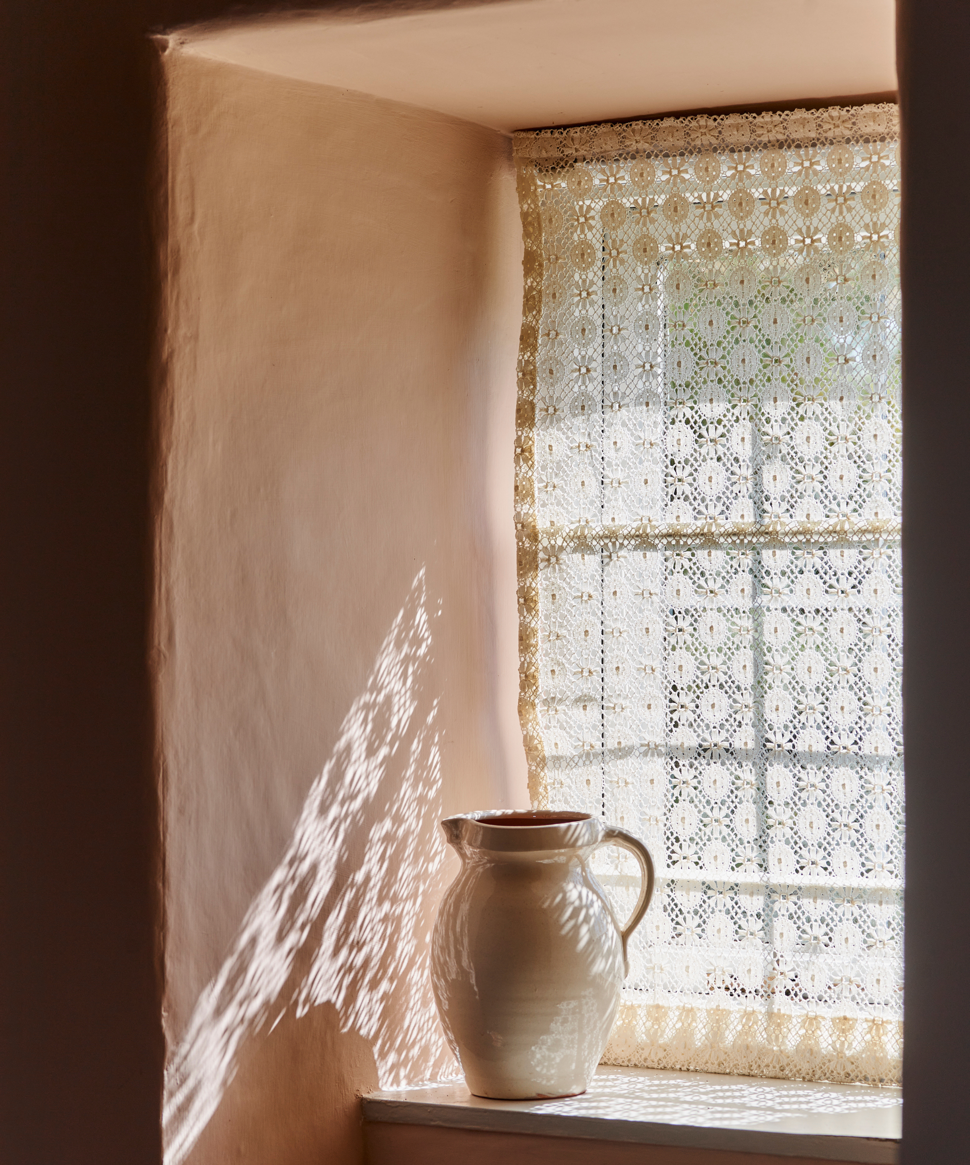 a window sill with a carafe and a lace curtain