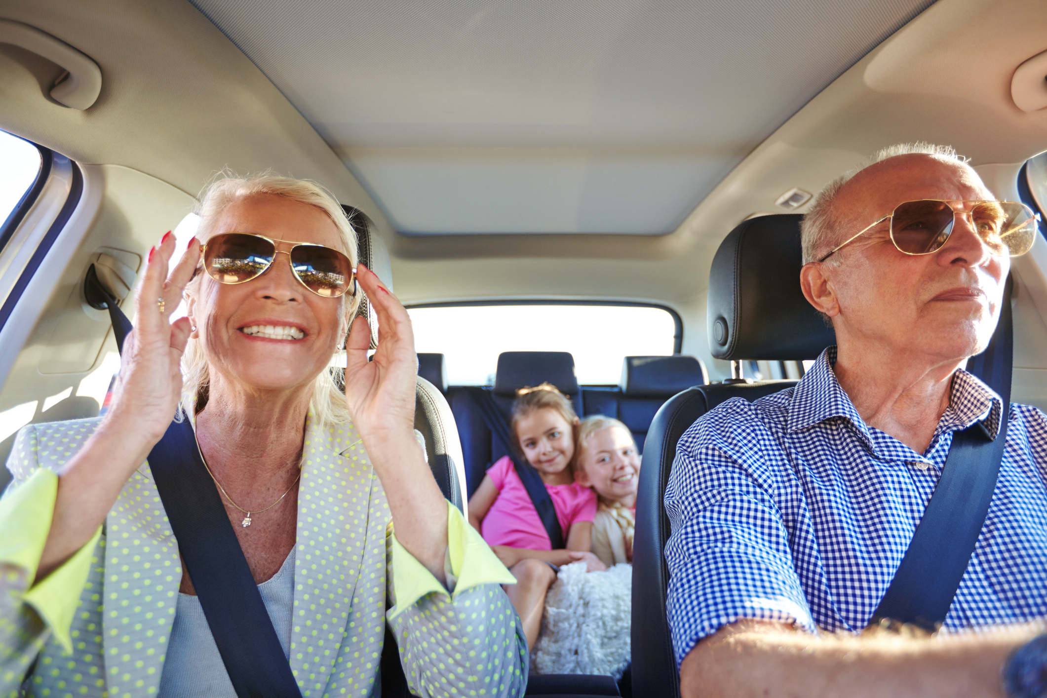 A senior couple driving in a car with their grandchildren.