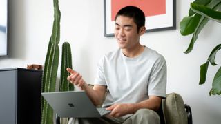 A man sat on a sofa next to plants with a Microsoft Surface Laptop Go 2