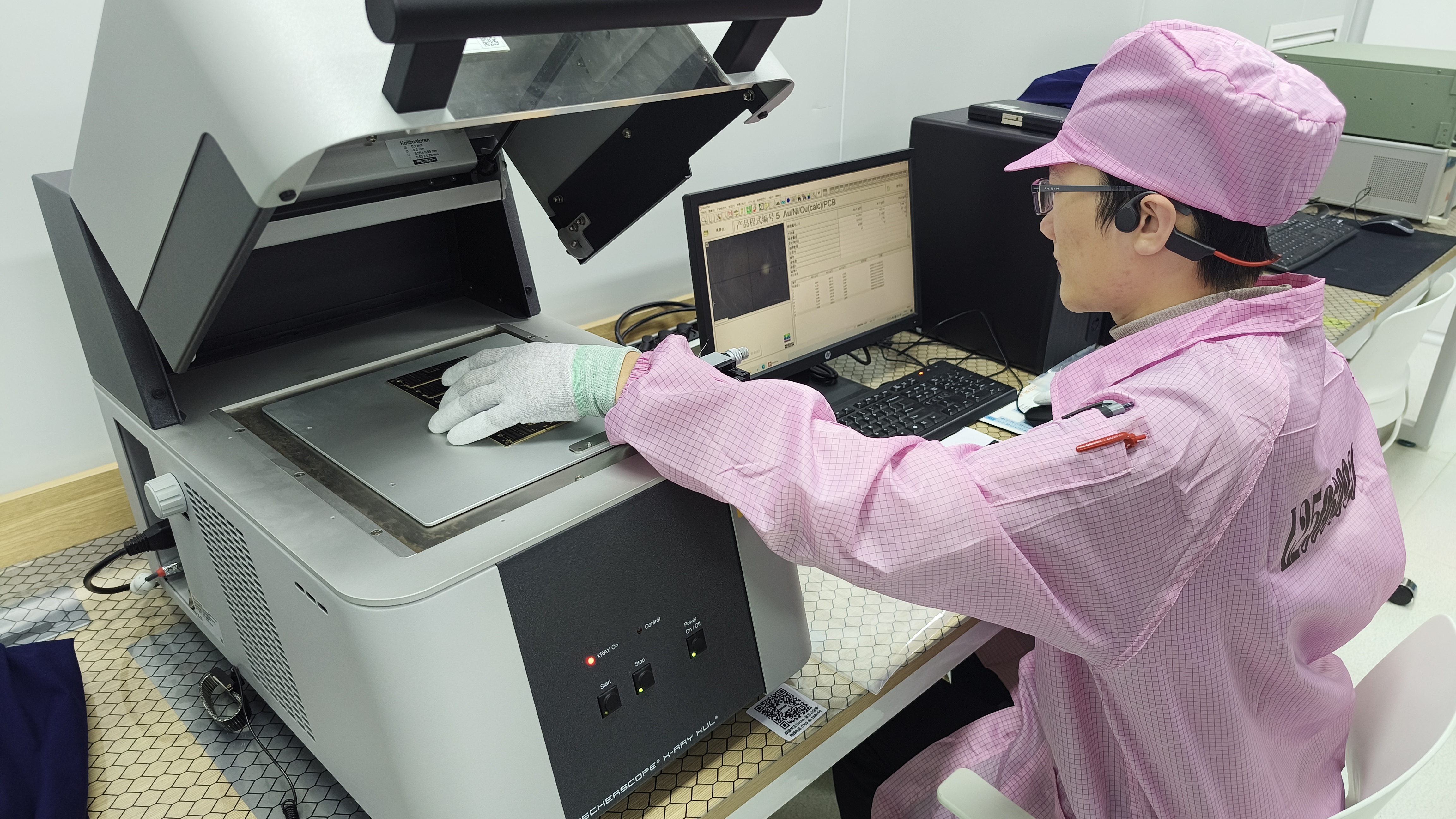 A person in a pink cleanroom suit and cap uses a gloved hand to position a component inside a FISCHERSCOPE X-RAY measurement system.