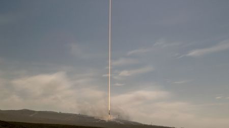 A daytime time lapse exposure of a rocket launch lifting off into partially cloudy sky.