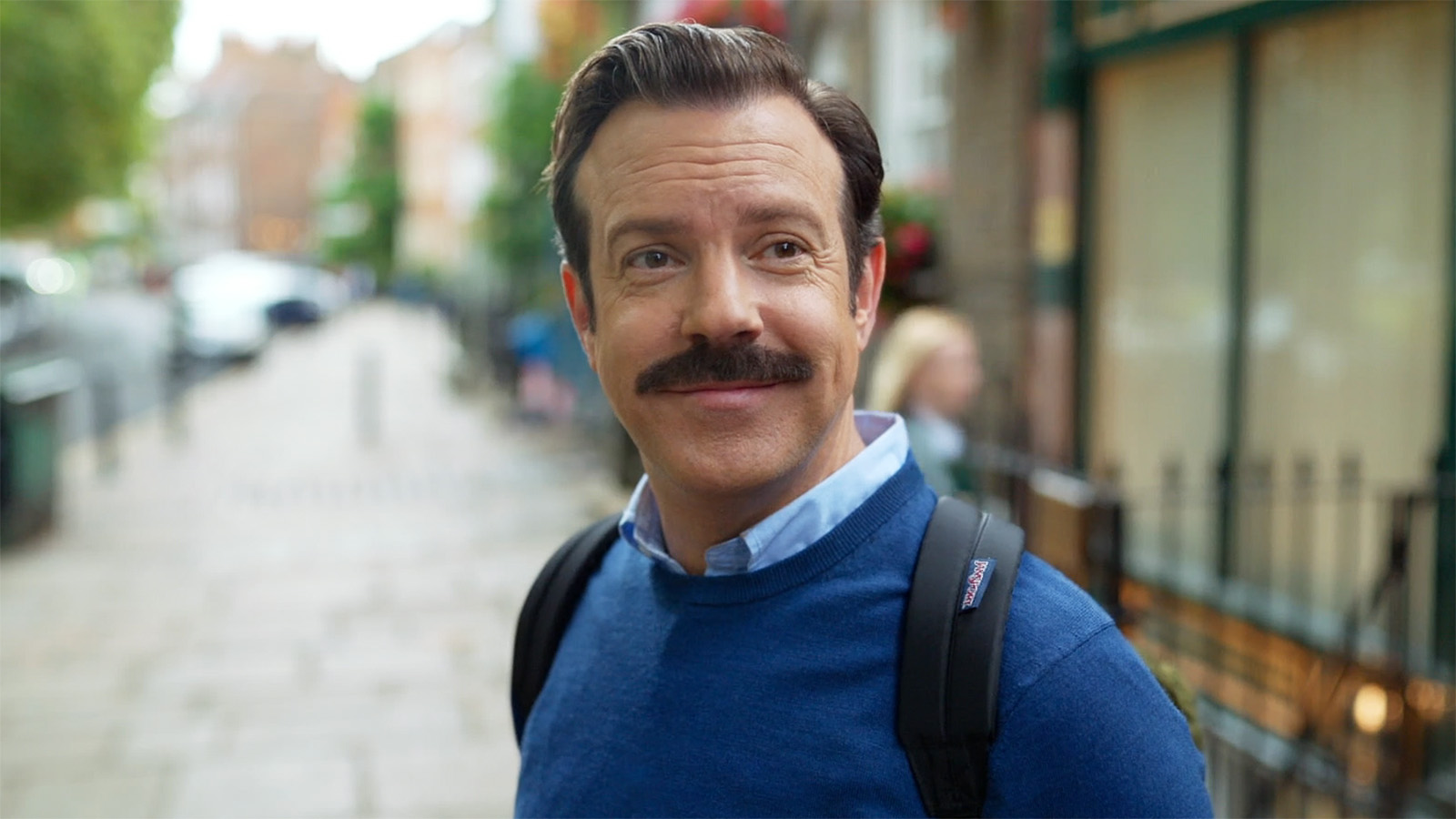 A close-up of Ted smiling as he stands on a street in Ted Lasso season 4 episode 2