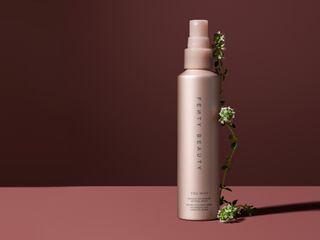 a bottle of fenty beauty's you mist setting spray in front of a plain backdrop