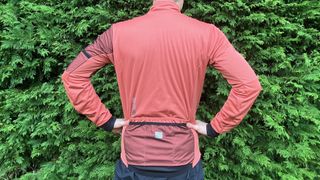 Rear view of man wearing Sportful Supergiara gravel jacket in front of hedge