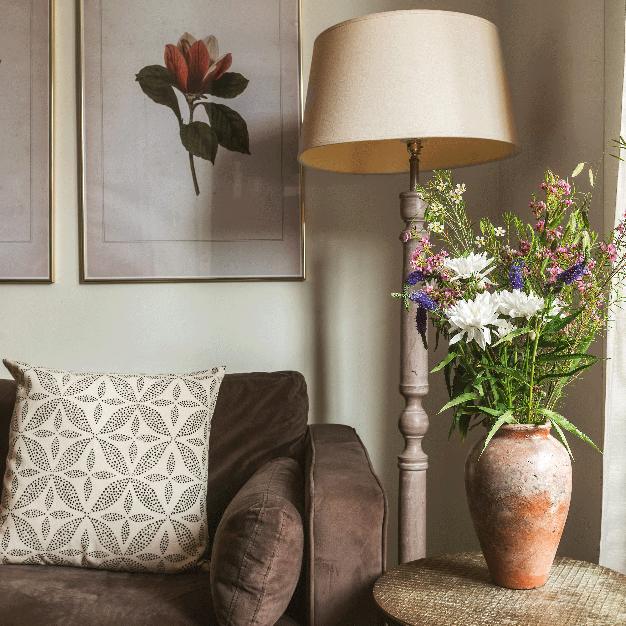 a living room with a brown sofa, floor lamp and a side table with an urn of flowers