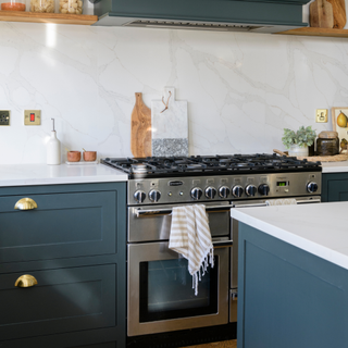 Silver gas oven with dark blue cupboards and white countertop