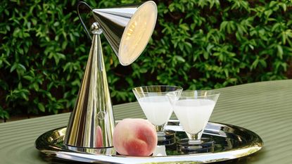 A portable chrome colored lamp on a silver tray with two glass shots and a peach
