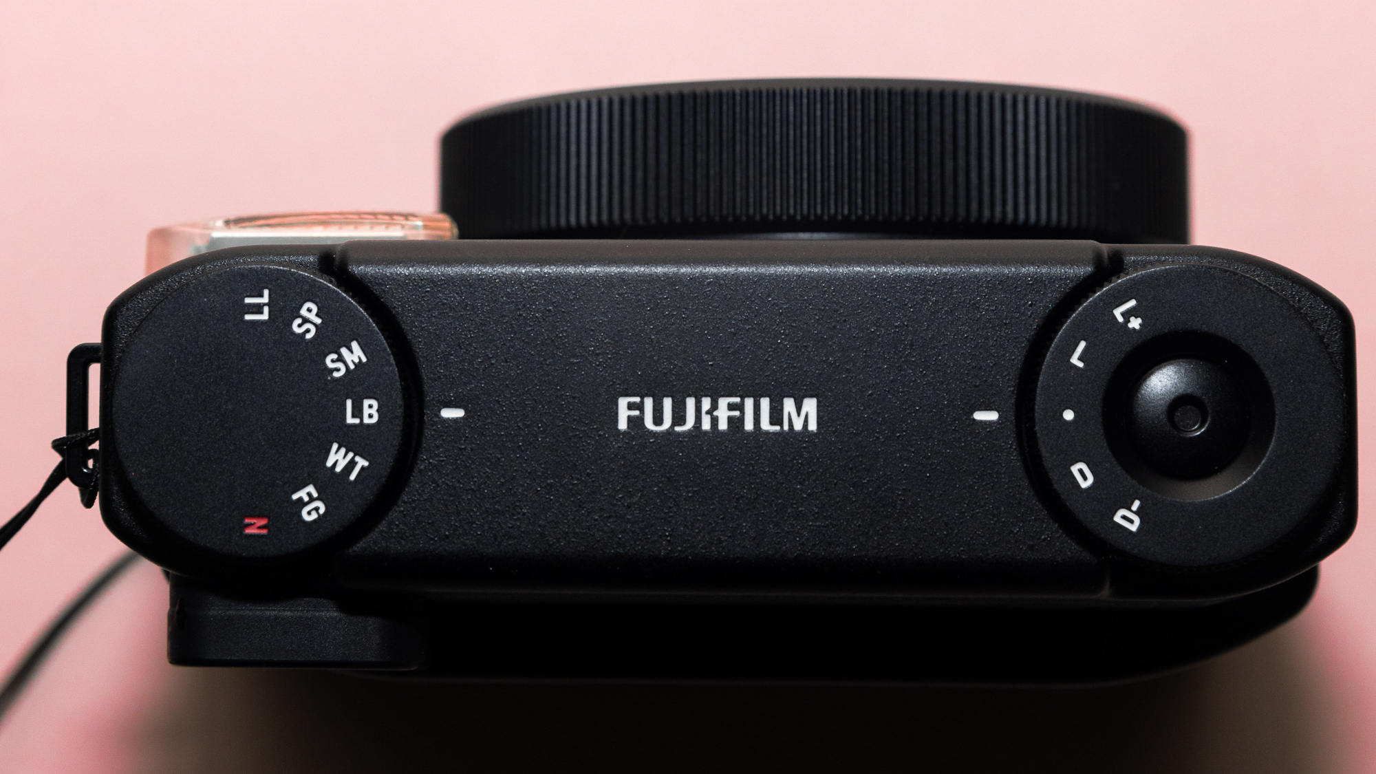 A photograph of the Fujifilm Instax mini 99 in black, set against a pink background.