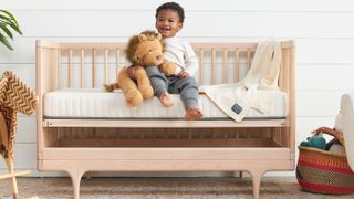 Image shows a little boy smiling while sat on the Avocado Green Eco Organic Crib mattress in his cot