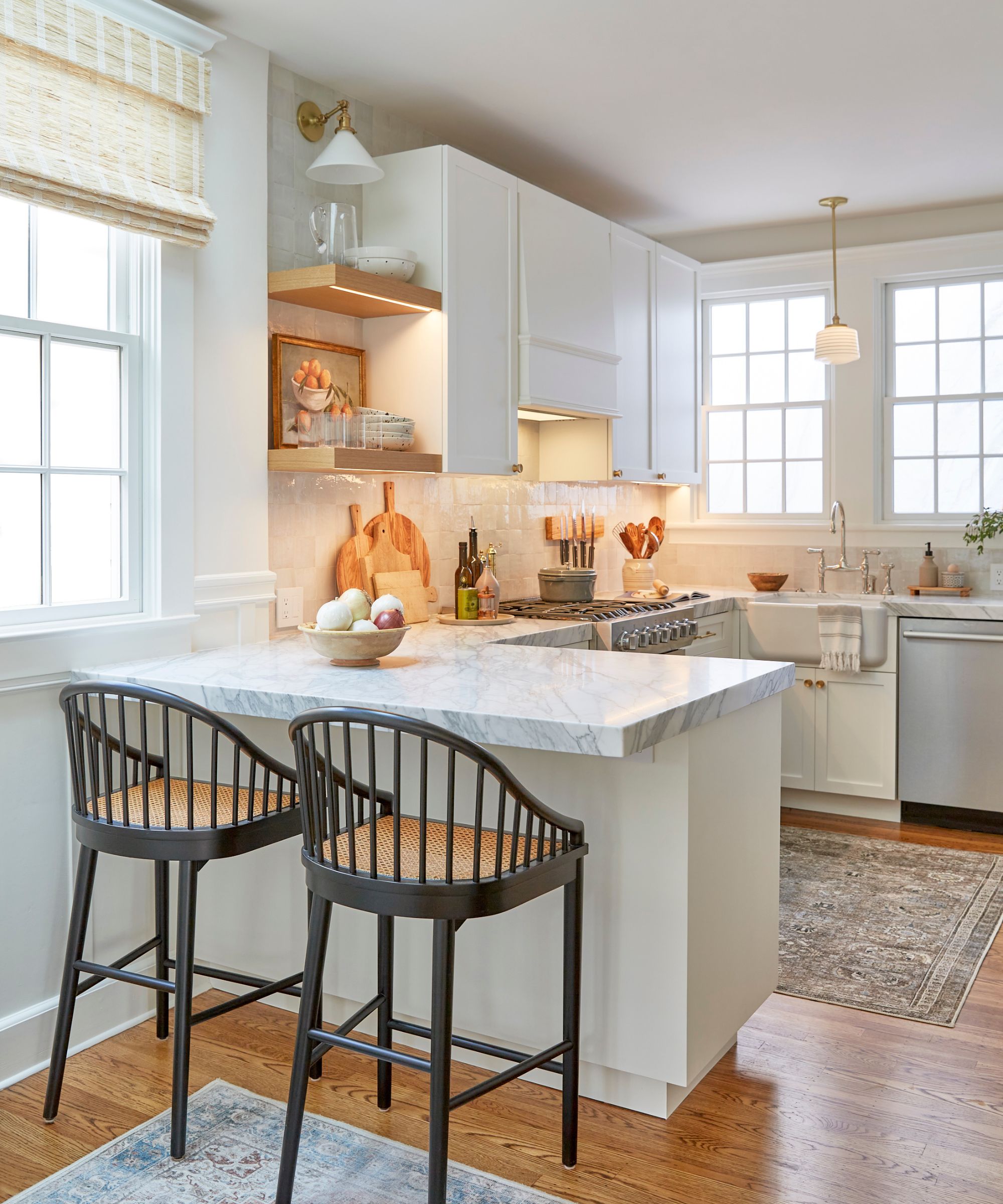 A small white kitchen with a peninsula layout, marble countertops, wooden floating shelves, and elegant lighting