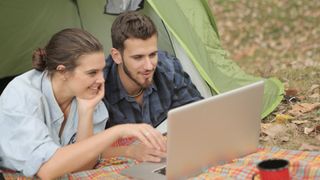 Couple sat in a tent, using one of the best travel laptops