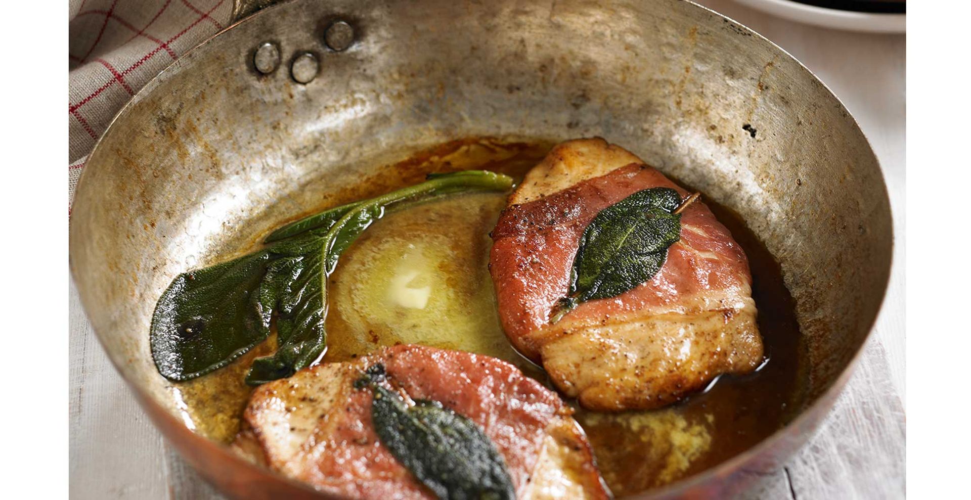 A copper pan cooking chicken breasts wrapped in bacon to show things you should never pour down drainsn