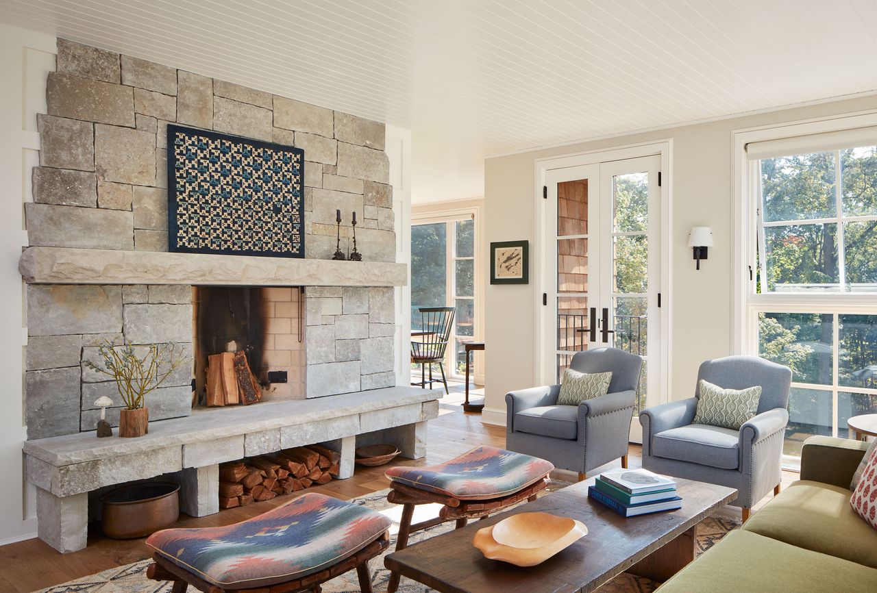 bright living room white paneled ceiling stone fireplace large windows green sofa pale blue armchairs twin kilim stools