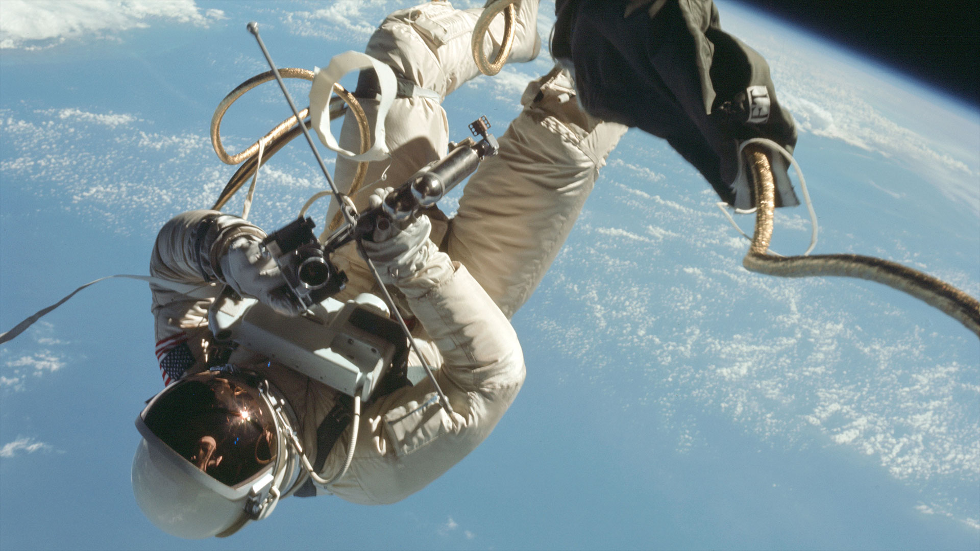 an astronaut in a white spacesuit floats in the vacuum of space backdropped by Earth