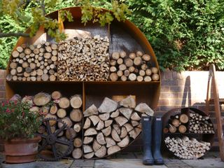 large circular metal log store on a patio filled with logs
