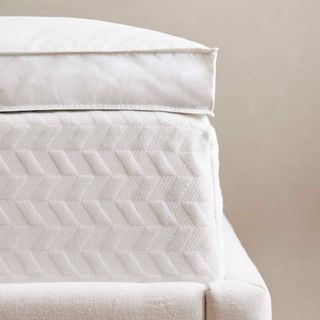 Corner of the Quince Luxe Downtop Featherbed Mattress Topper against a beige wall.