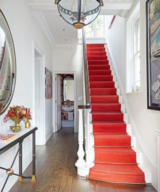 Hallway with wooden floor, elaborate cornice and staircase with red carpet.