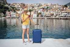 Young smiling woman standing on pier with suitcase and using smartphone