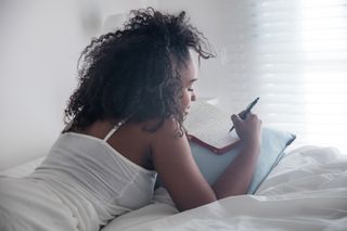 A woman lays in bed while writing in her journal